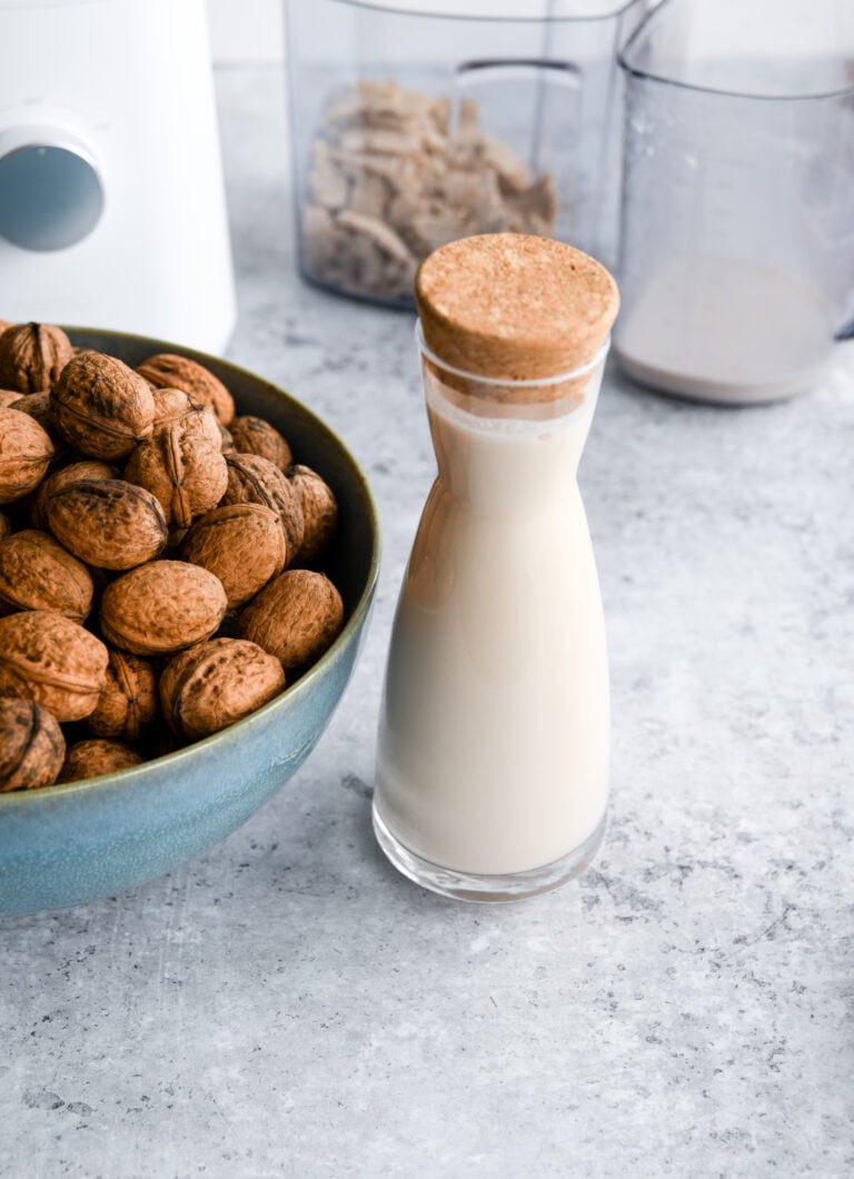 a blue bowl of walnuts next to a glass bottle full of walnut milk