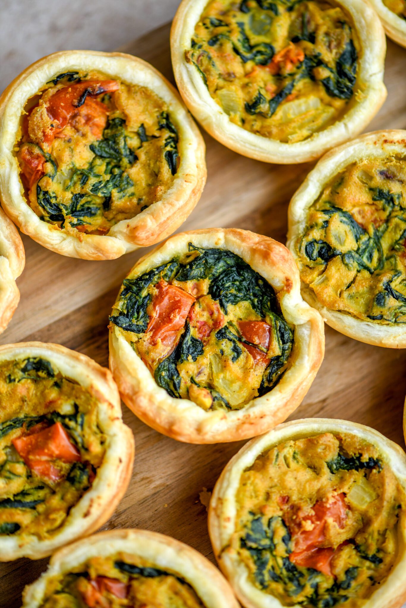 12 mini quiches on a wooden board with a green cloth napkin
