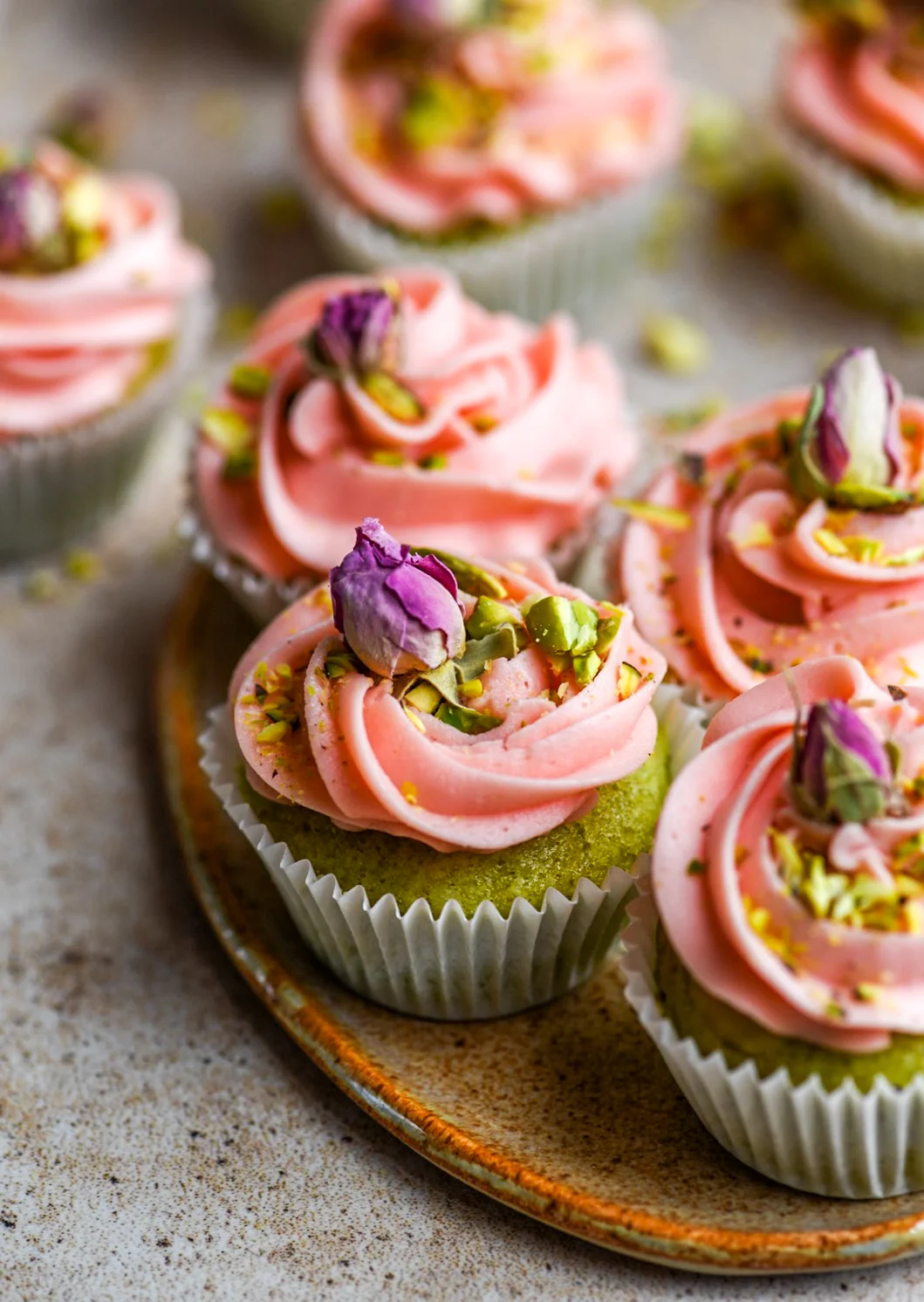 green mini cupcakes with pink buttercream topped with chopped pistachios and dried rose buds